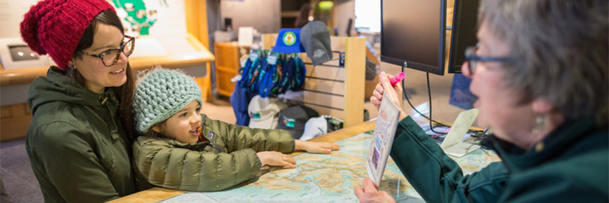 A mother and daughter look at a map with a Parks Canada employee.