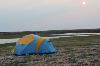 Une tente sur la toundra avec une rivière en arrière-plan.