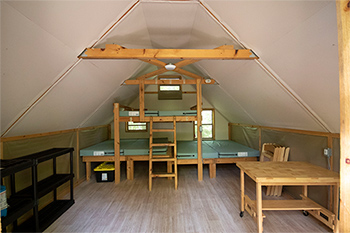 Intérieur de l'oTENTik montrant des lits superposés pouvant accueillir 6 personnes, ainsi qu'une table et des chaises.