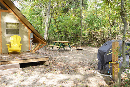 Extérieur du camping oTENTik montrant le barbecue et la table de pique-nique.