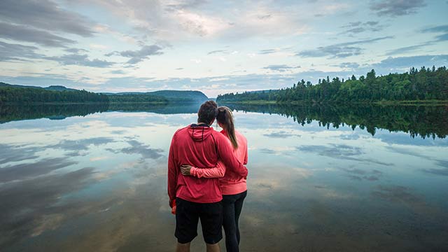 Deux adultes se tenant par la taille regardent un lac calme bordé de la forêt au parc national de la Mauricie.