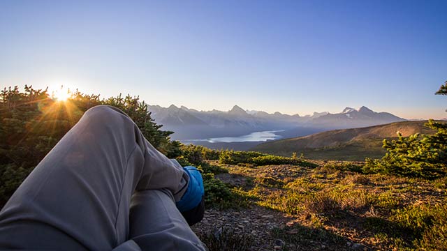 Prise de vue où l'on voit les jambes du photographe qui est assis et contemple un paysage de montagne en arrière-plan lors du lever de soleil au parc national Jasper.