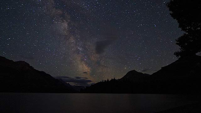 Un ciel étoilé au dessus d'un lac avec des montagnes en arrière-plan au parc national des Lacs-Waterton.